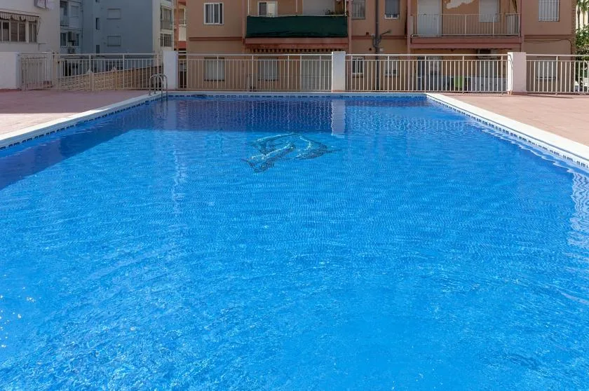 An outdoor swimming pool with apartment buildings and railings in the background.