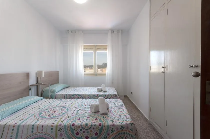A bright bedroom with patterned bedding, bedside tables, and a window.