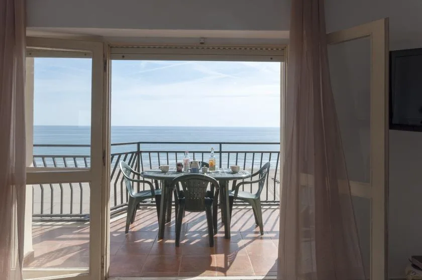A balcony dining area overlooks the sea, with a table and chairs beside the railing.