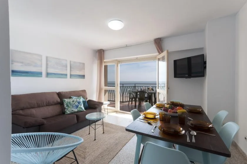 A living and dining area opens onto a balcony overlooking the sea.