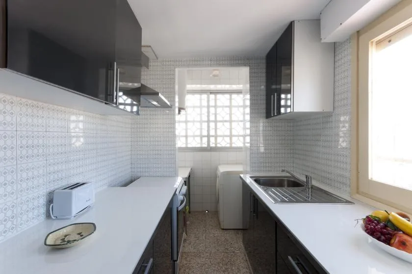A narrow kitchen with tiled walls, countertops, and a window at the far end.