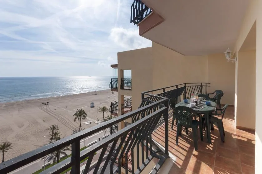 A balcony dining area overlooks a sandy beach and the ocean.