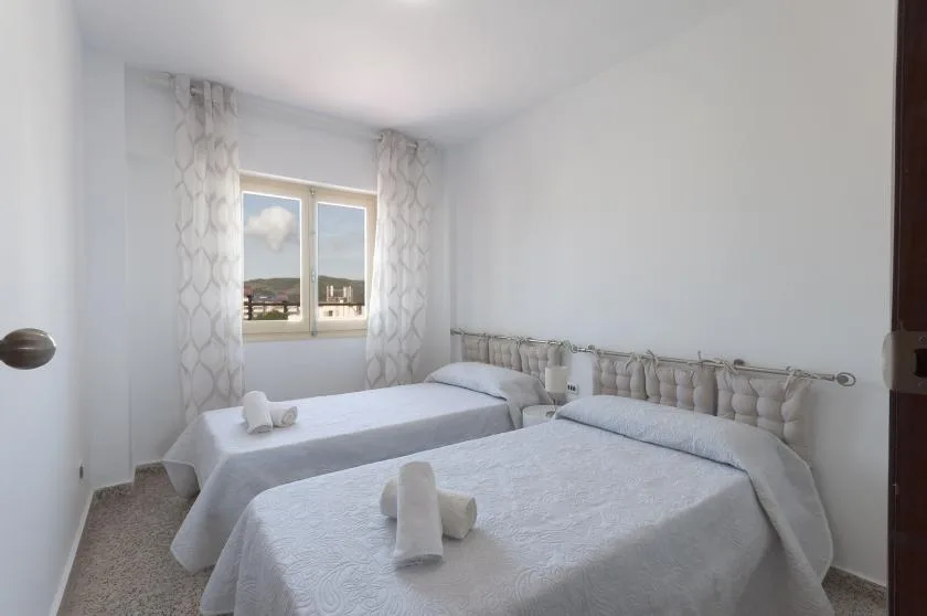 A bright bedroom with two beds and a window framed by patterned curtains.