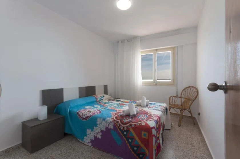 A bedroom with a bed covered by a colorful patterned bedspread and a window.