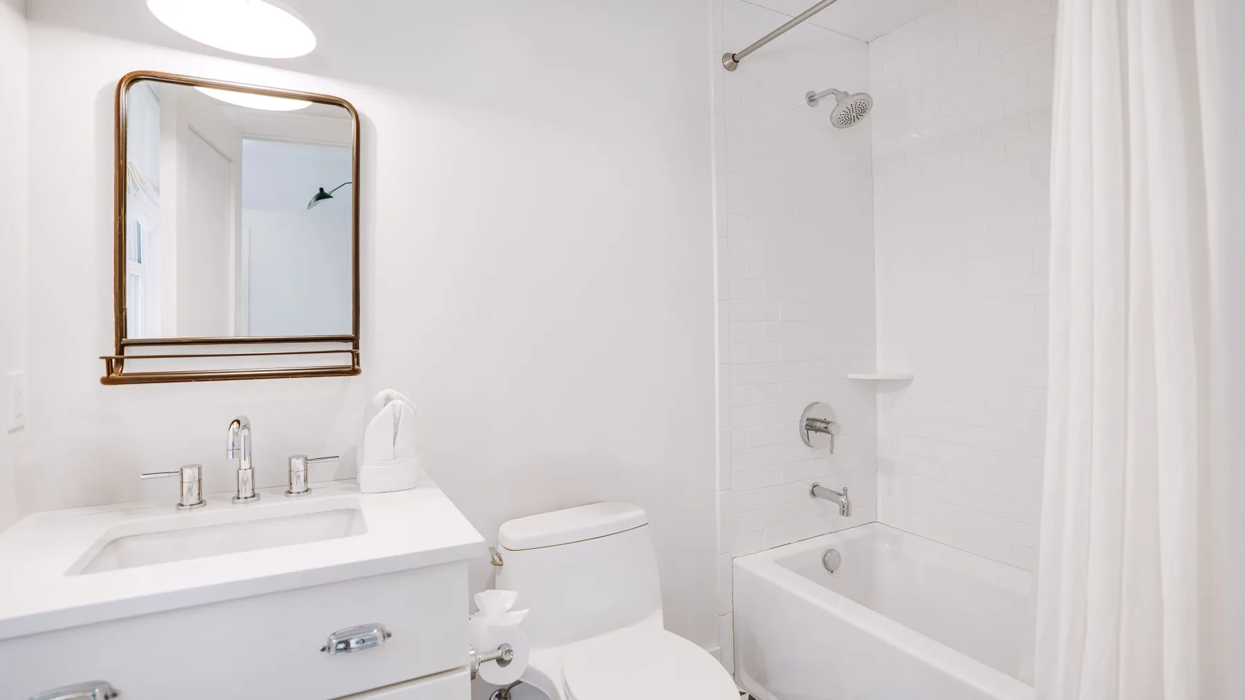 Un baño luminoso con lavabo, espejo, inodoro y bañera con ducha.