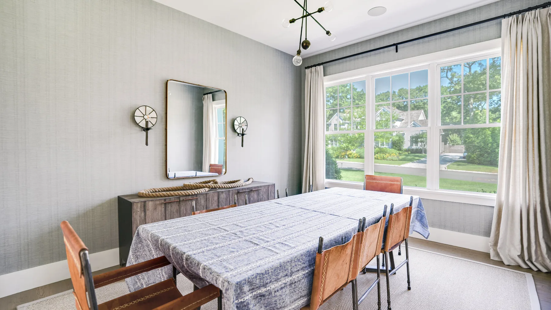 Un comedor con una mesa larga y grandes ventanas con vistas a zonas verdes.