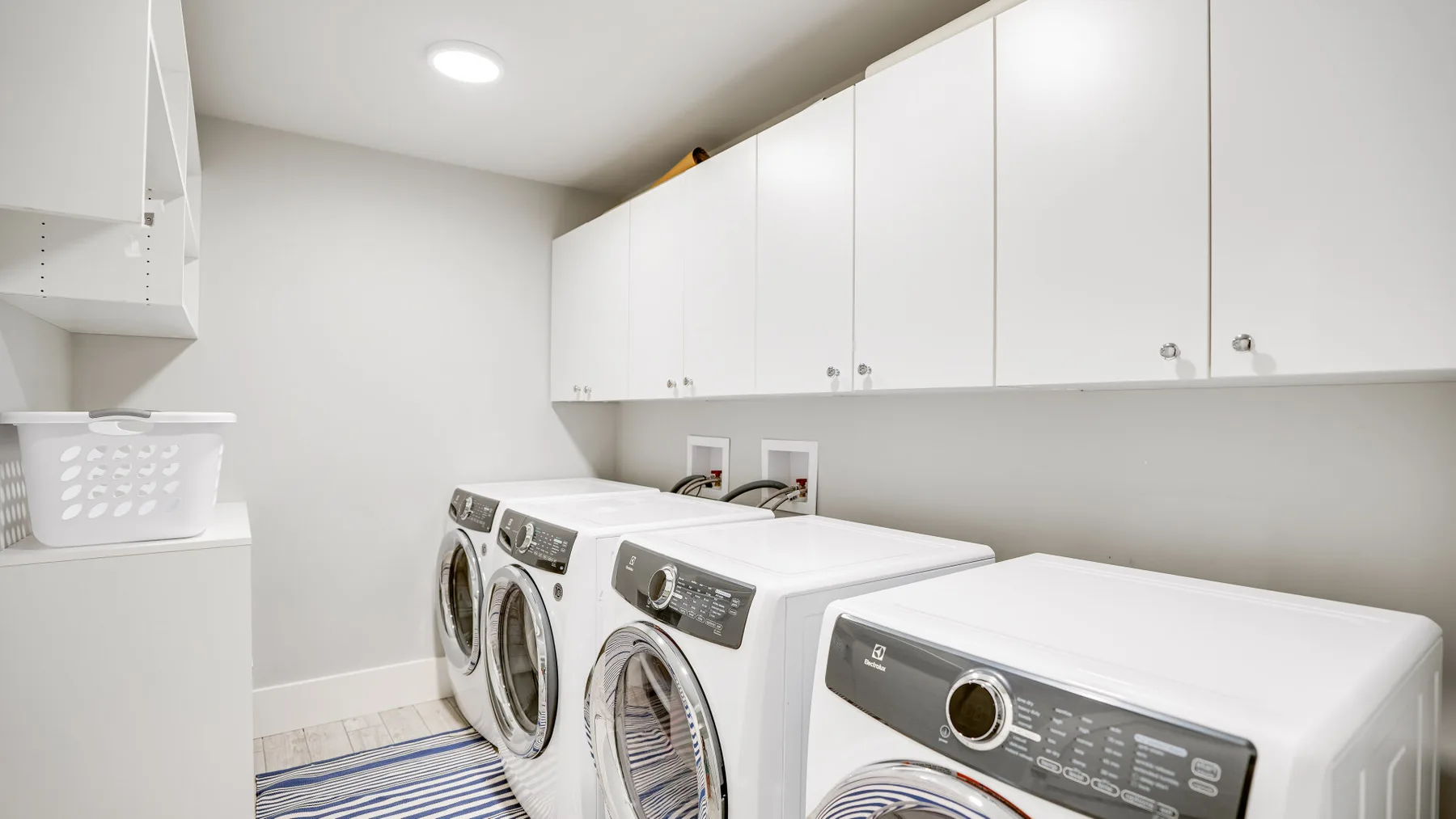 Un cuarto de lavandería con lavadoras debajo de armarios blancos.