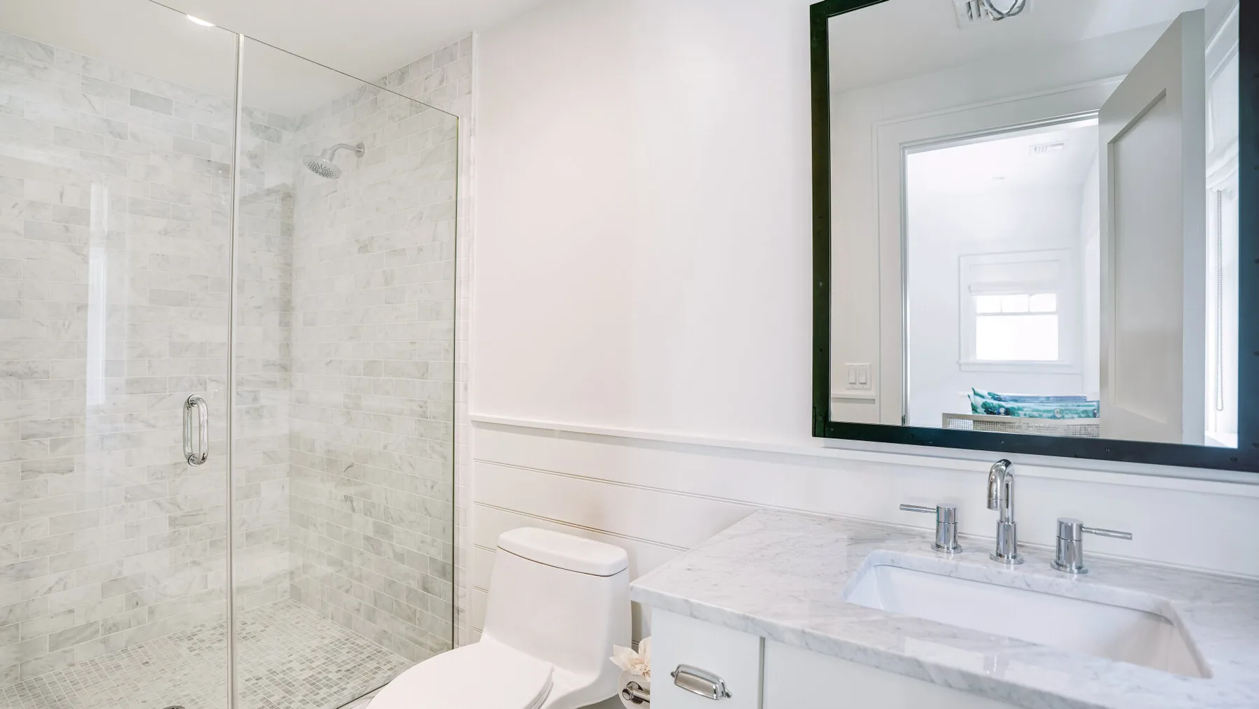 Un baño luminoso con ducha de vidrio, inodoro y lavabo.