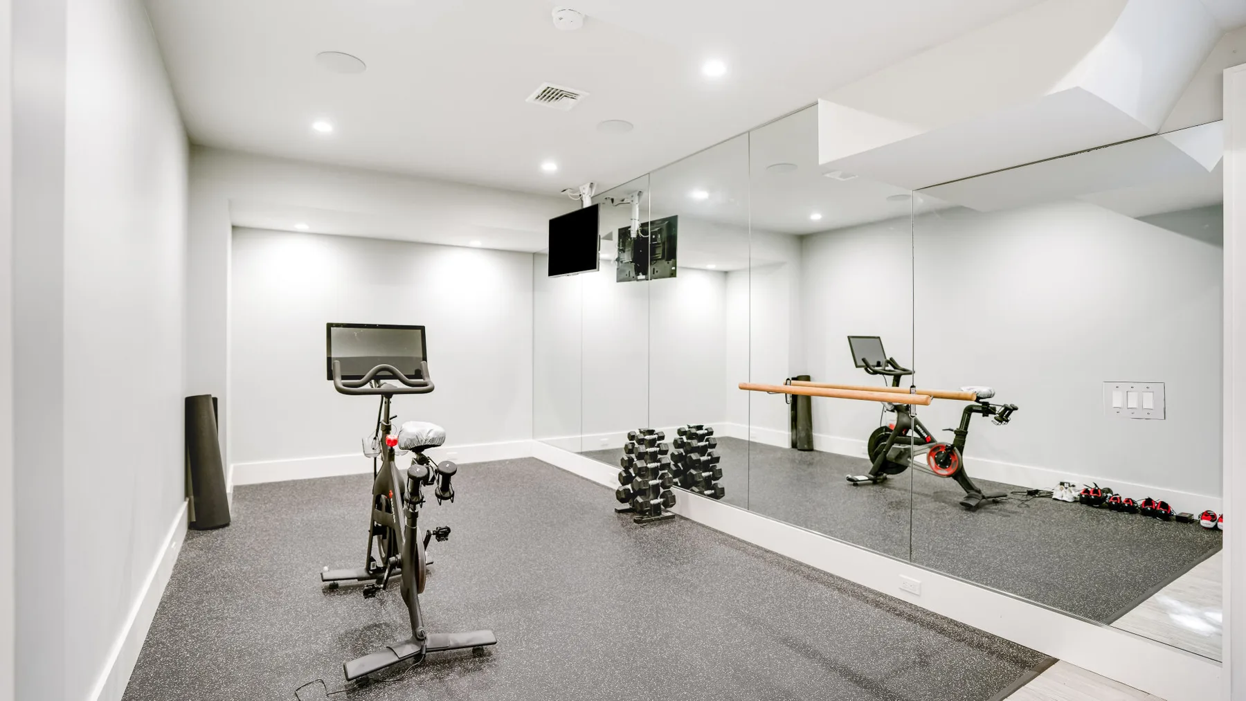 Una sala de ejercicio luminosa con bicicletas estáticas y pesas junto a una pared con espejo.