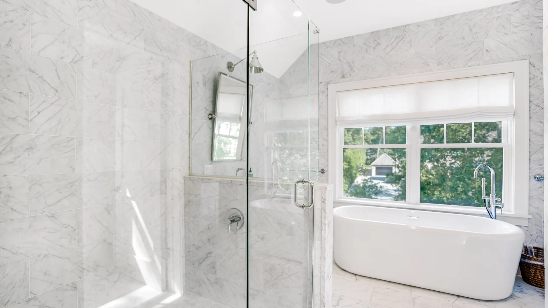 Un baño luminoso con una ducha de vidrio y una bañera exenta junto a la ventana.