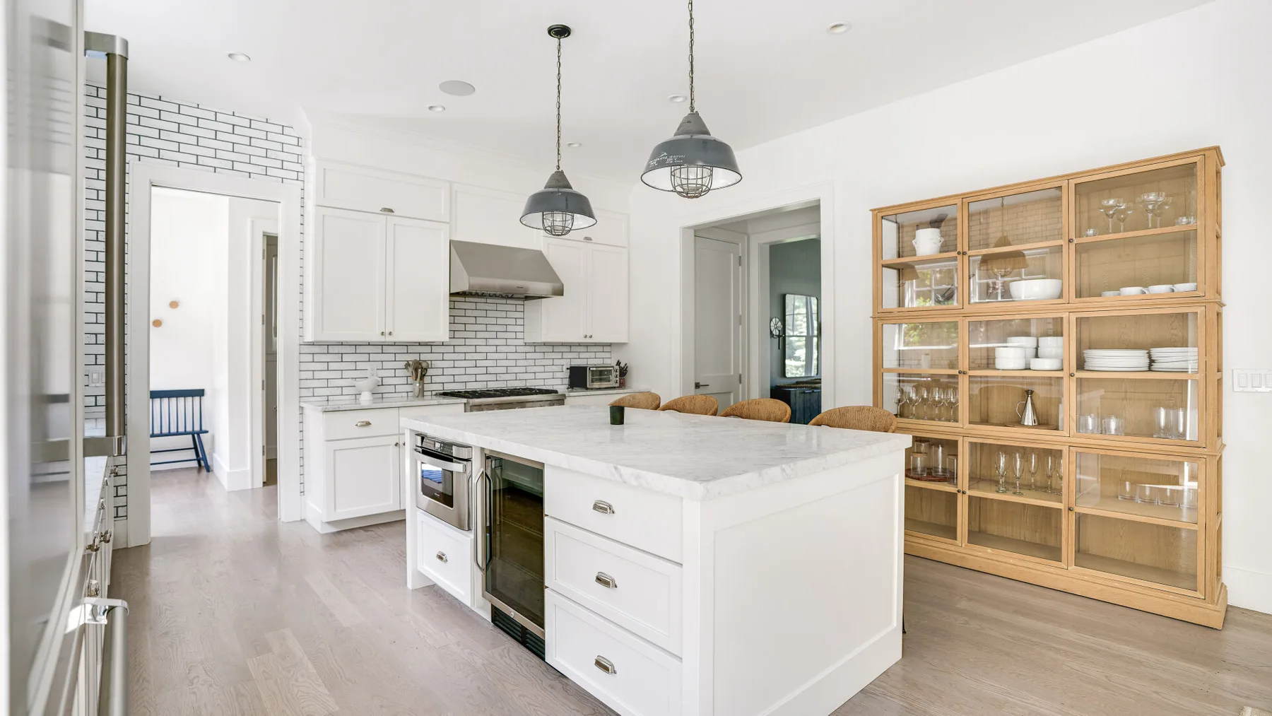 Una cocina luminosa con una isla central, gabinetes blancos y estanterías abiertas.