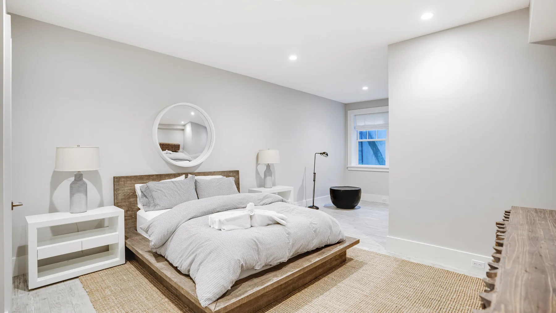Un dormitorio con una cama baja, ropa de cama blanca y mesitas de noche a juego.
