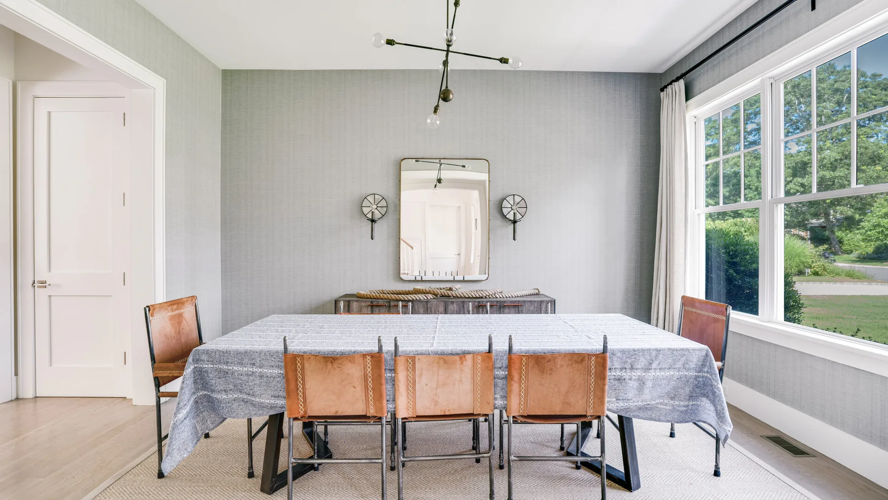 Un comedor con una mesa larga y sillas junto a grandes ventanas.