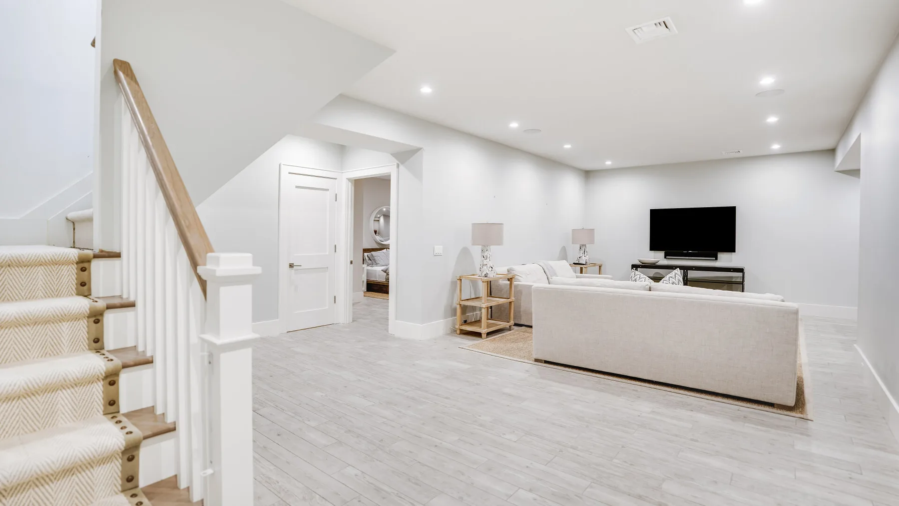Una luminosa sala de estar en el sótano con asientos, televisor y escaleras.