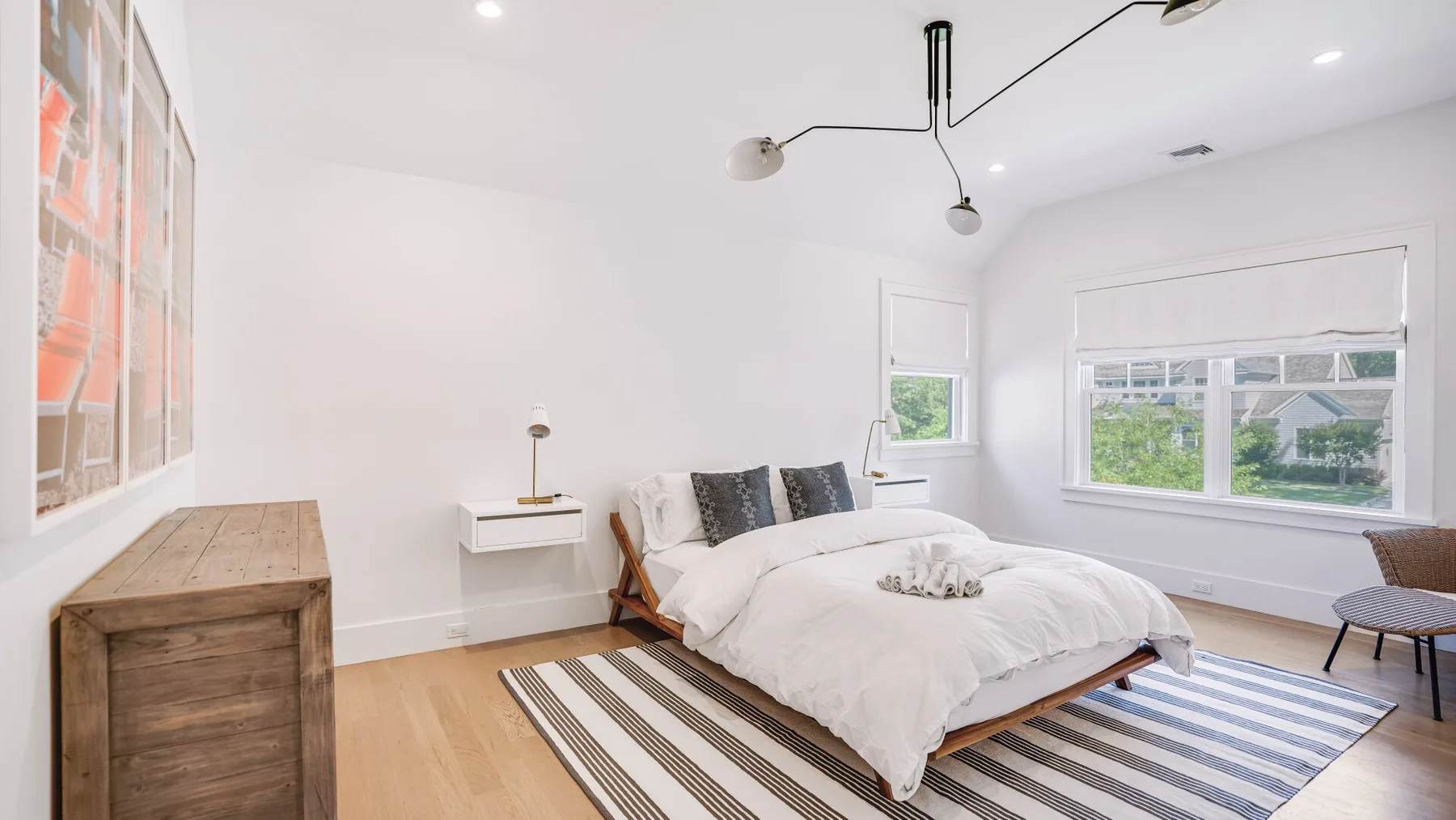 Un dormitorio luminoso con cama, alfombra a rayas y ventanas.