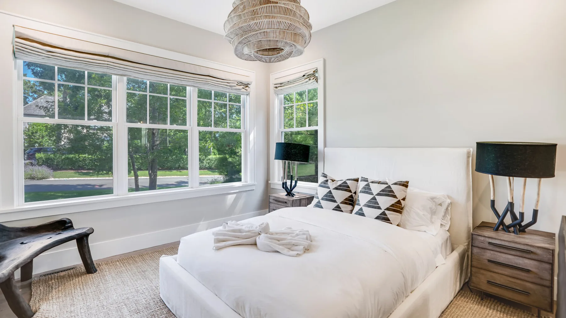 Un dormitorio luminoso con una cama blanca junto a grandes ventanas con vistas a la vegetación.