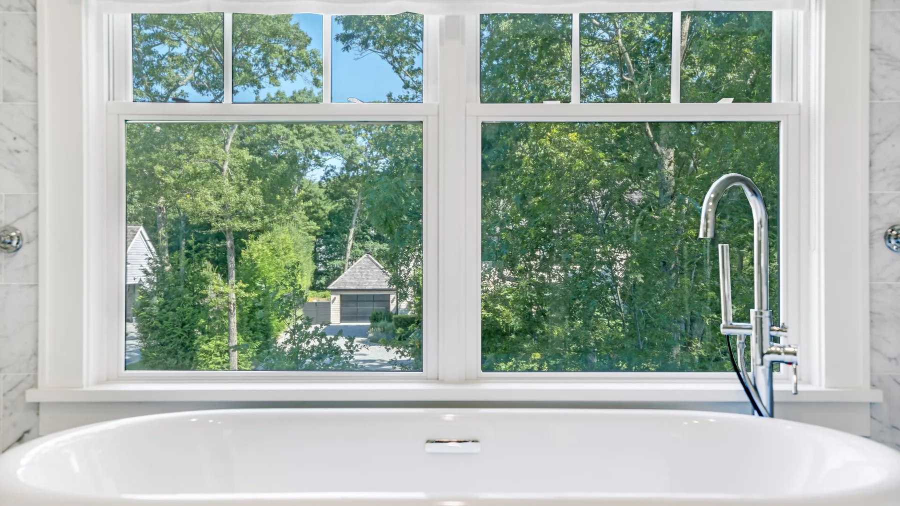 Una bañera está debajo de grandes ventanas con vistas a árboles frondosos.