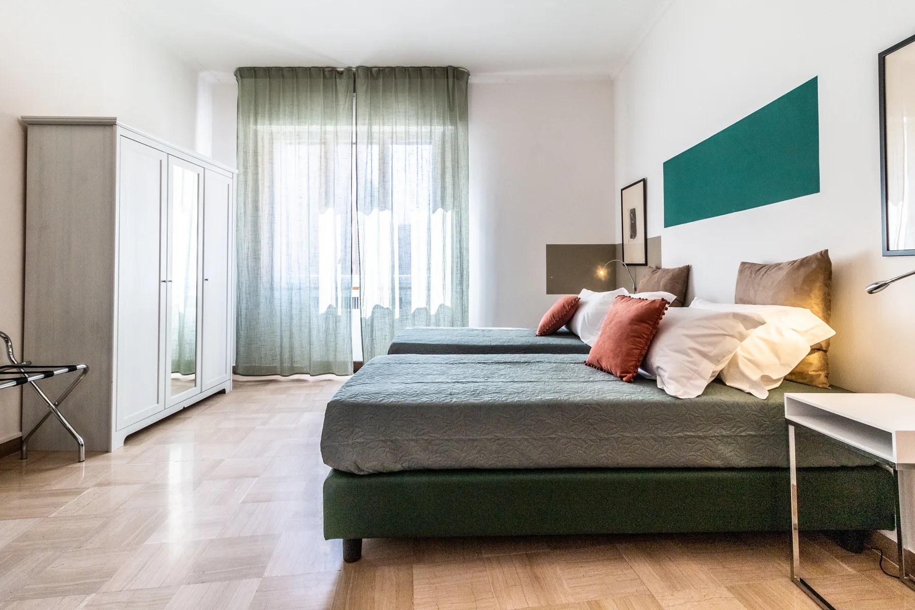 Un dormitorio luminoso con una cama grande, un armario y una ventana con cortinas translúcidas.
