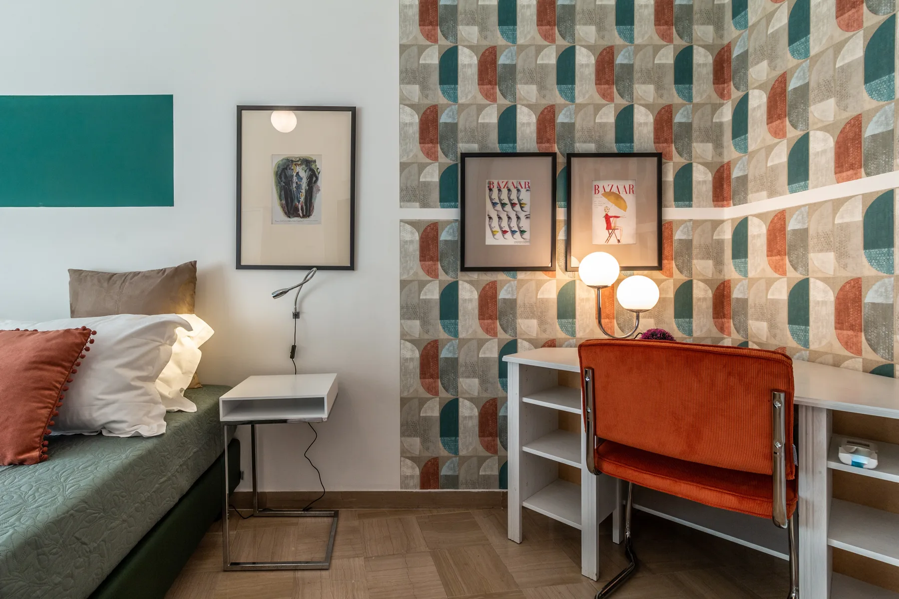Un dormitorio con zona de escritorio y una cama junto a una pared con papel pintado estampado.