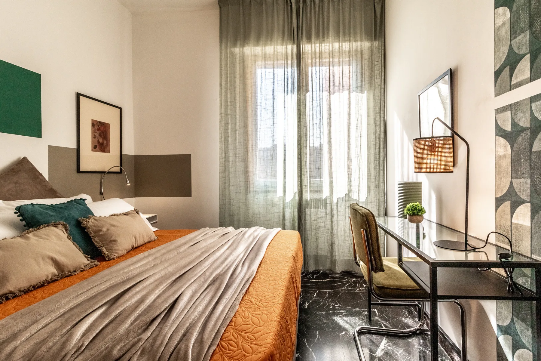 Un dormitorio con una cama junto a un escritorio y ventanas altas con cortinas.
