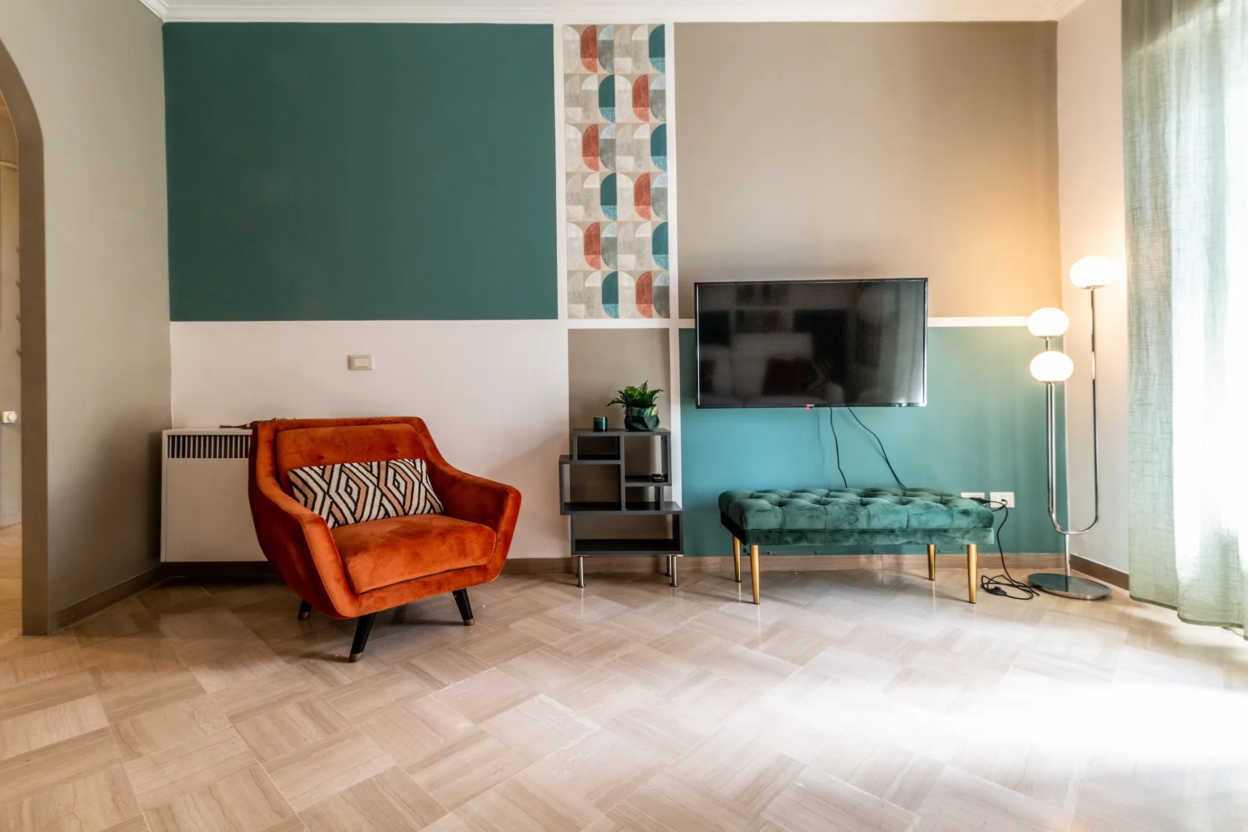 Una sala de estar con asientos coloridos, un televisor en la pared y ventanas altas.