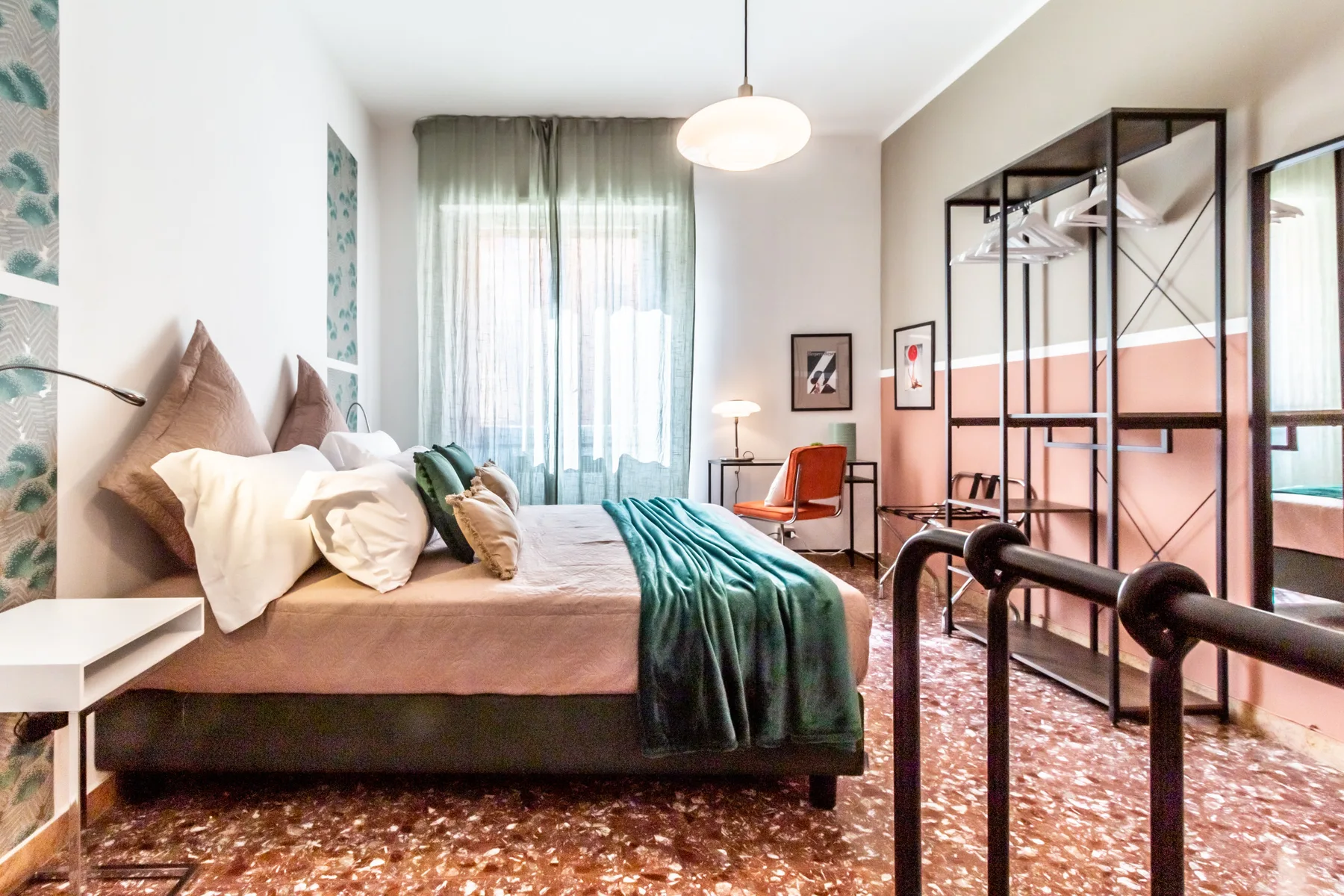 Un dormitorio con una cama, cortinas translúcidas y un perchero metálico negro.