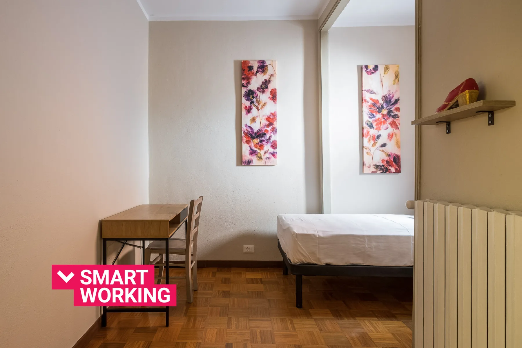 Un dormitorio con una cama, un escritorio pequeño y arte floral en la pared.