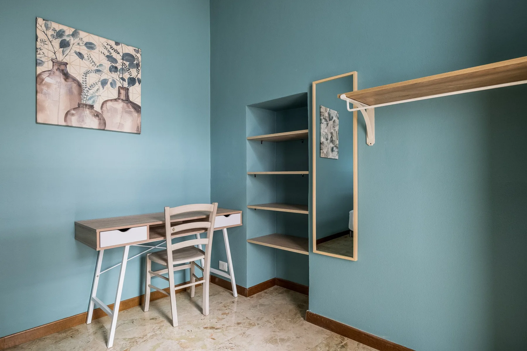 Una habitación pequeña con escritorio, silla, estantes y espejo de pared.