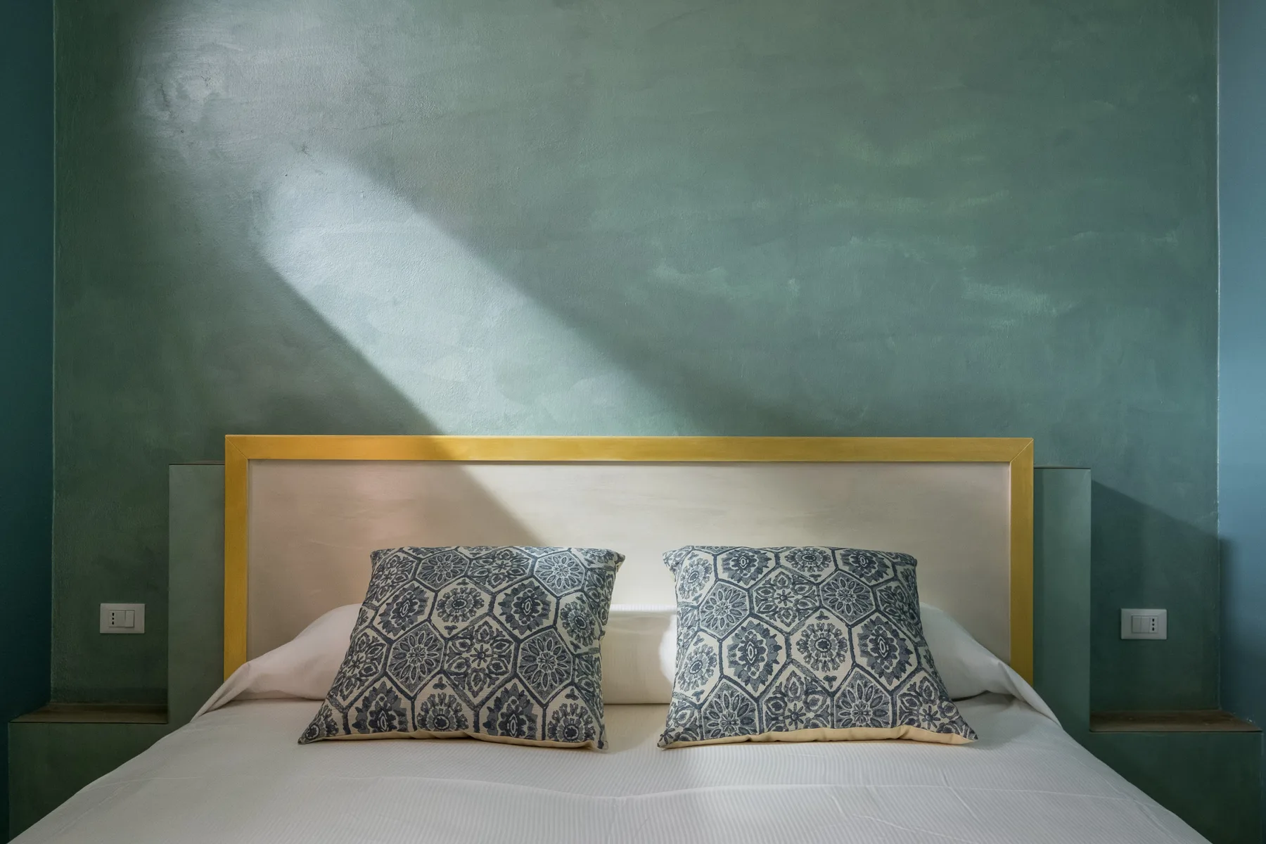 Un dormitorio con cojines estampados sobre una cama frente a una pared verde.