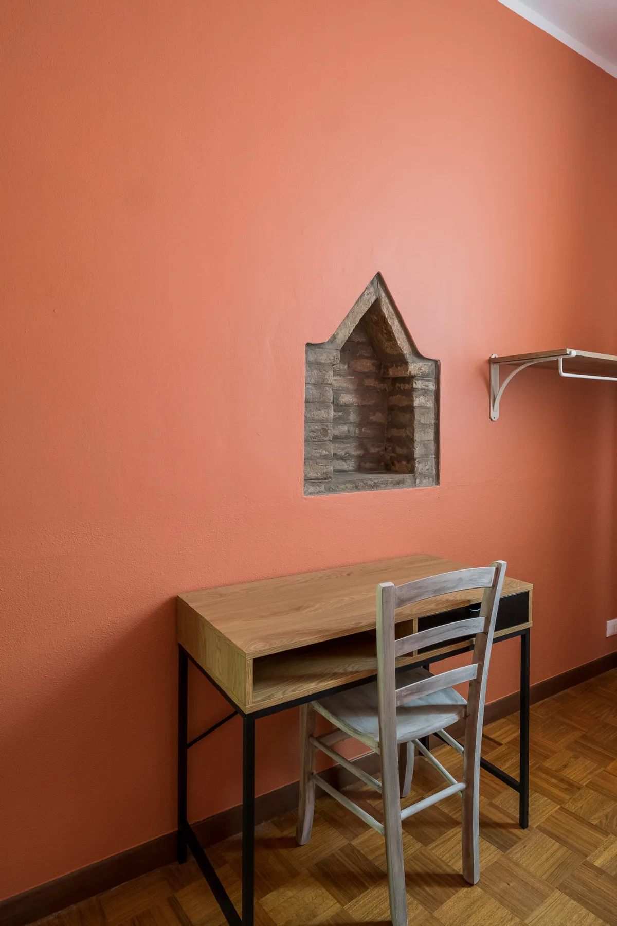 Un pequeño escritorio y una silla están junto a una pared color coral con un nicho empotrado.