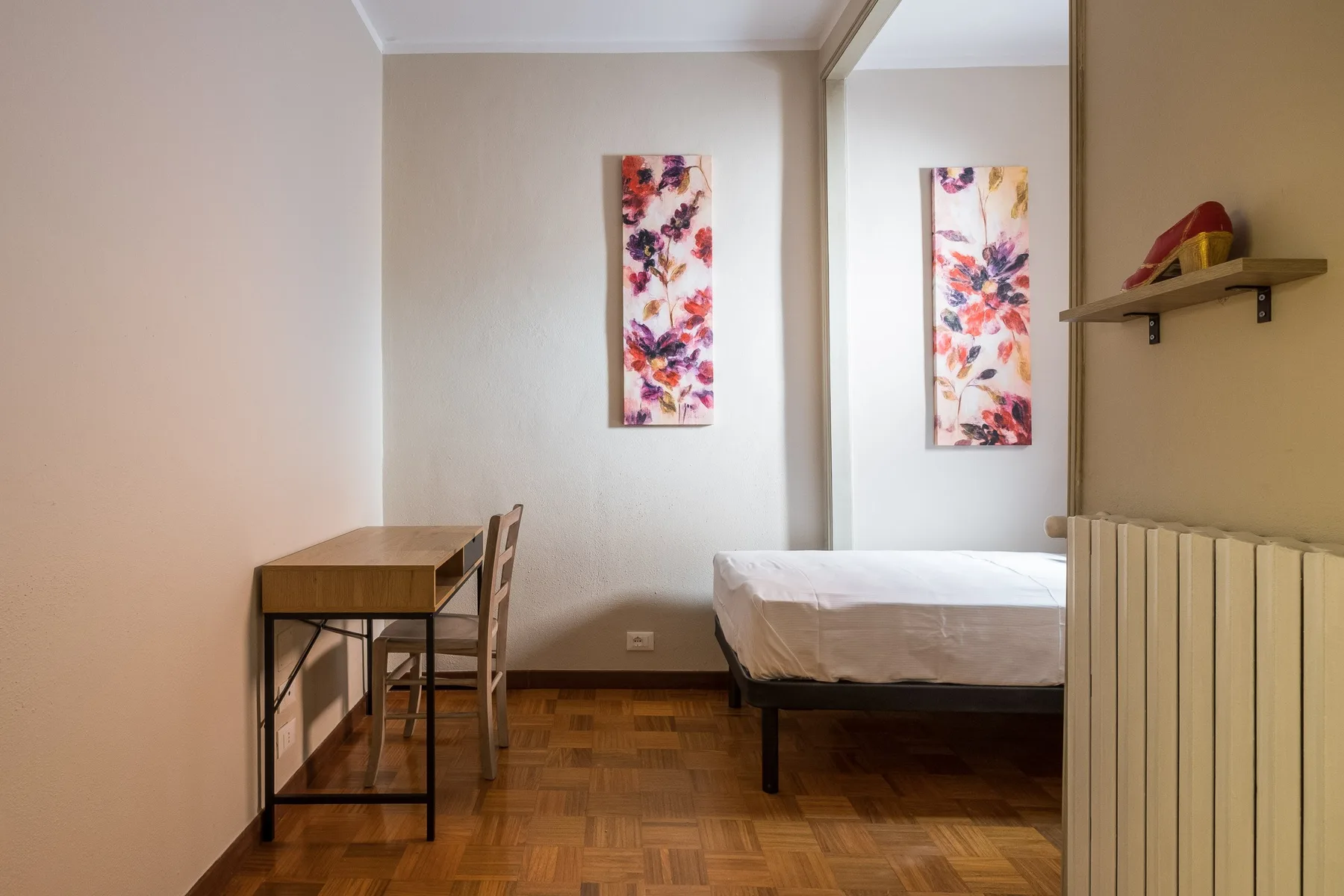 Un dormitorio con una cama, un escritorio pequeño y cuadros florales.