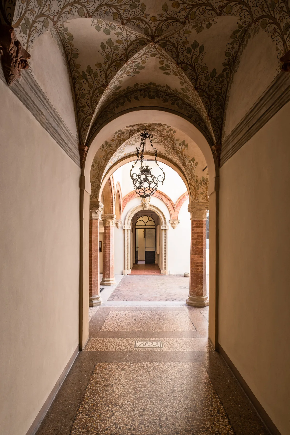 Un pasillo con arcos ornamentados conduce a un corredor luminoso con una lámpara colgante.