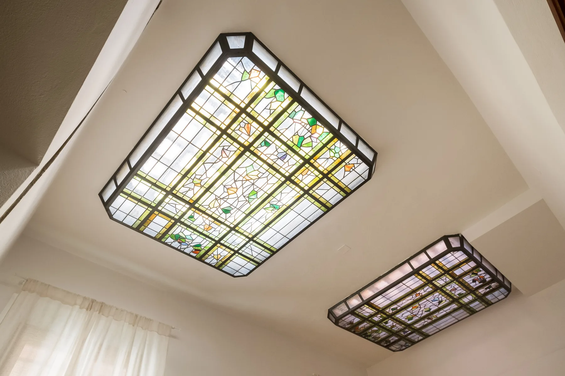 Techo de una habitación con dos lámparas de vidrieras y una ventana con cortinas.