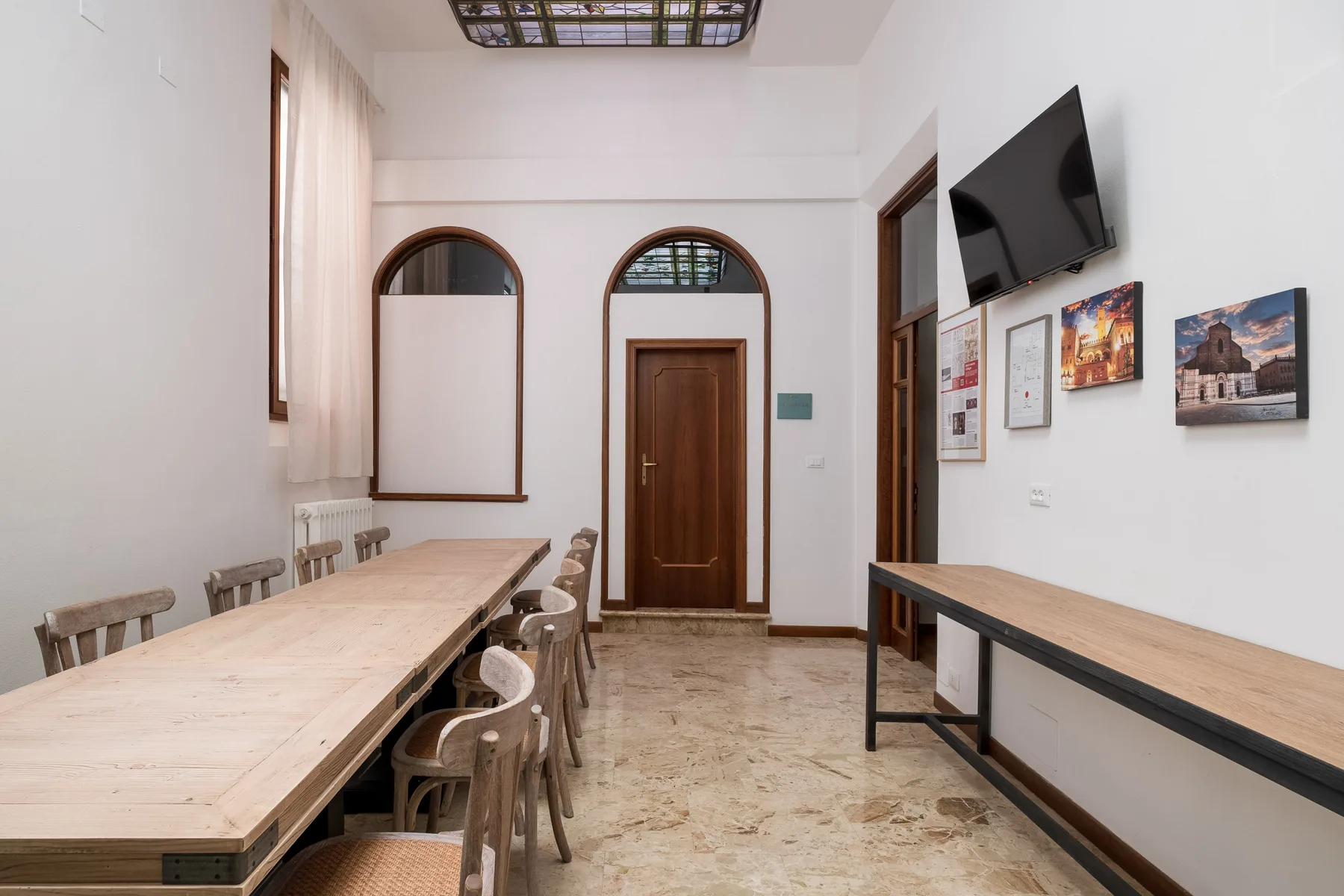 Un comedor luminoso con una mesa larga de madera, asientos y cuadros enmarcados.