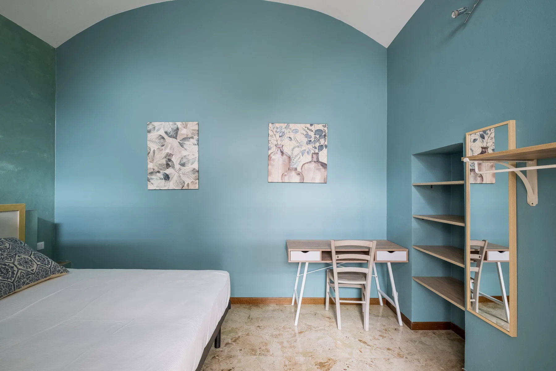 Un dormitorio con una cama, un escritorio y estanterías abiertas junto a paredes verde azulado.