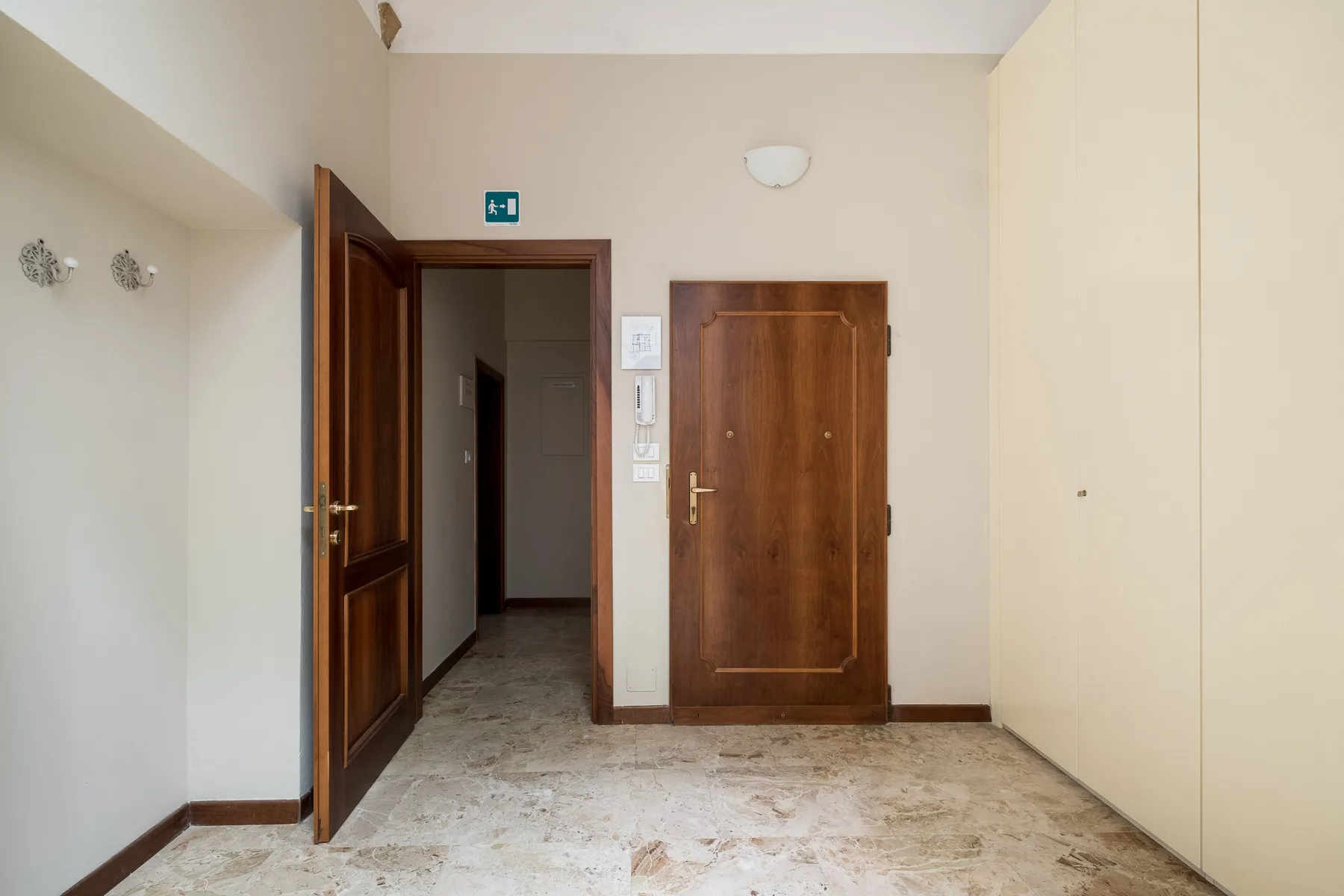 Un pasillo interior con puertas de madera y suelo de baldosas claras.