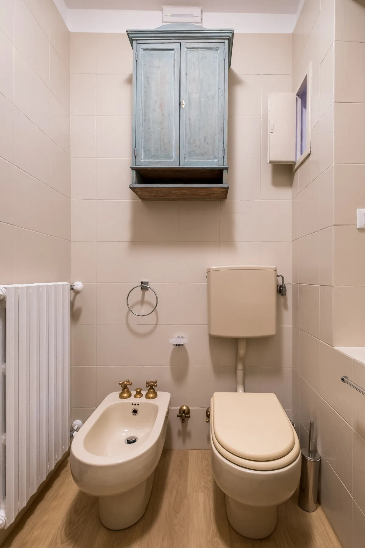 Un baño de azulejos con un armario de pared, bidé e inodoro.