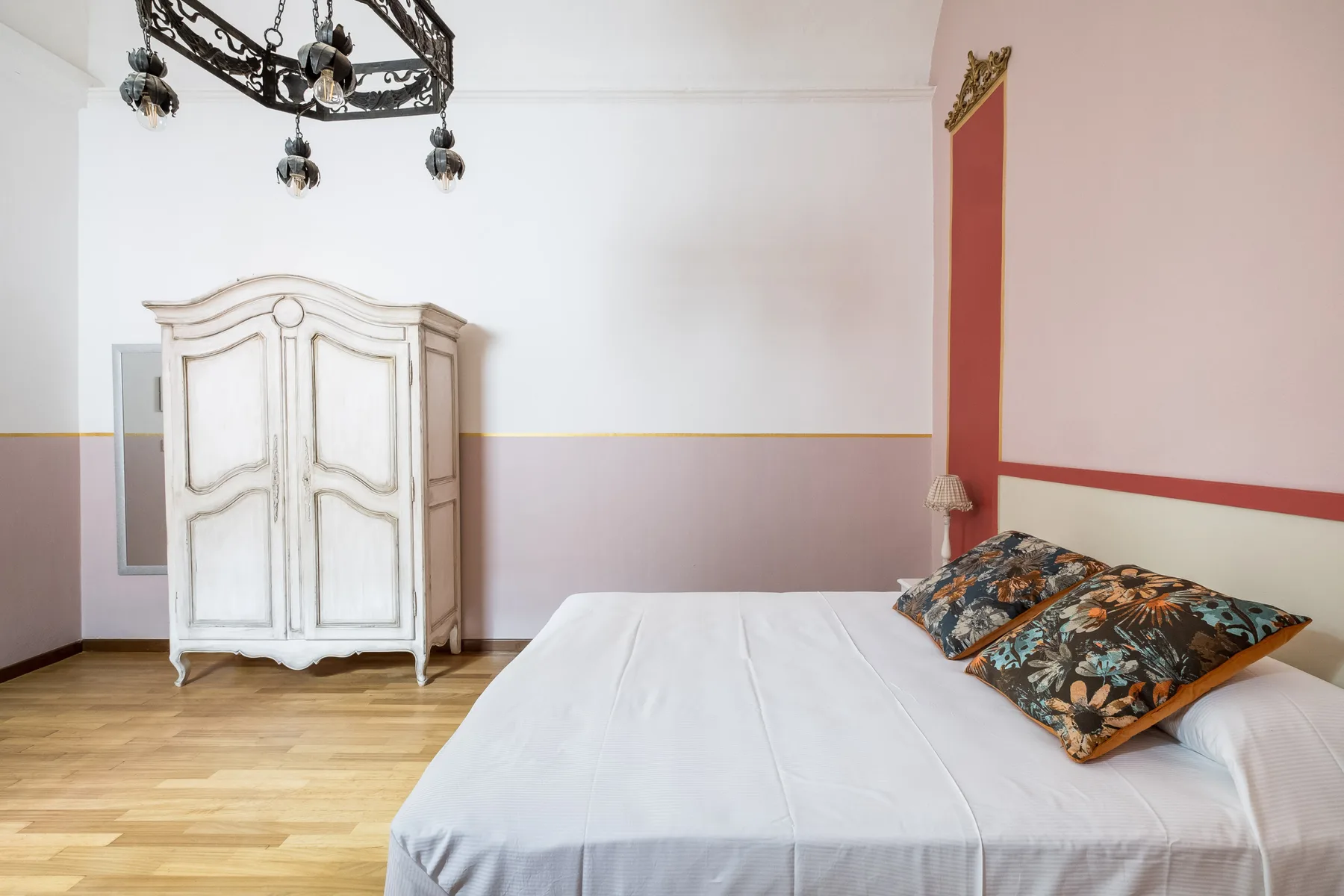 Un dormitorio con una cama, almohadas florales y un armario blanco.