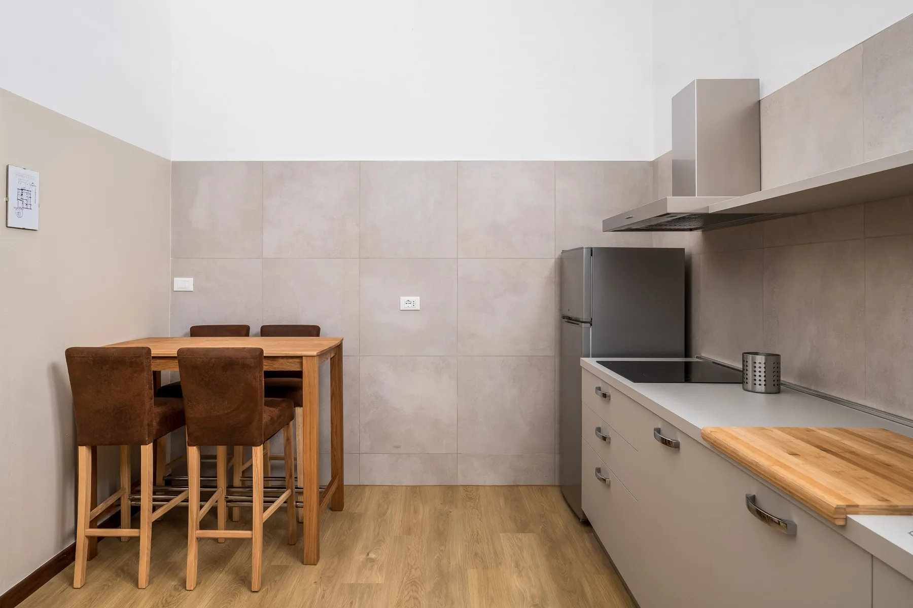 Una cocina con zona de comedor, mesa de madera, asientos y armarios claros.