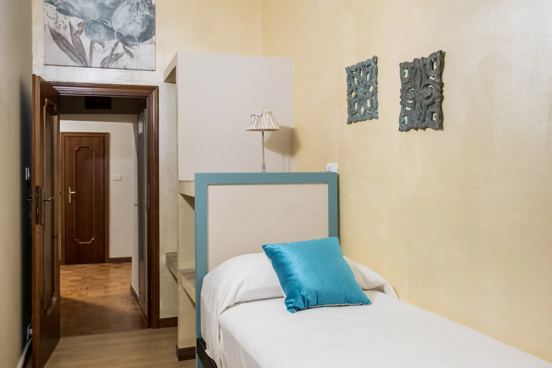 Un dormitorio con una cama individual, un cojín azul y cuadros en la pared.