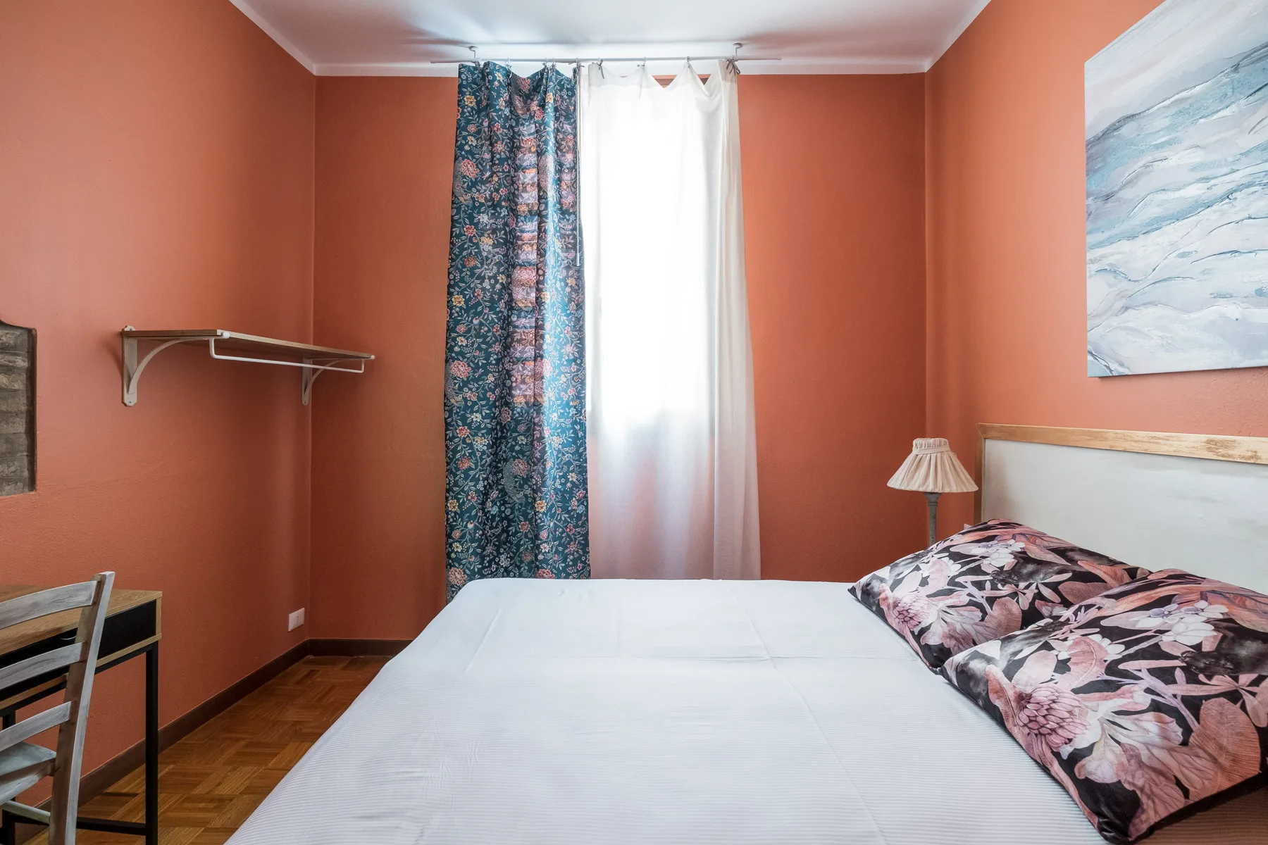 Un dormitorio con una cama junto a una ventana con cortinas y una pequeña lámpara de noche.