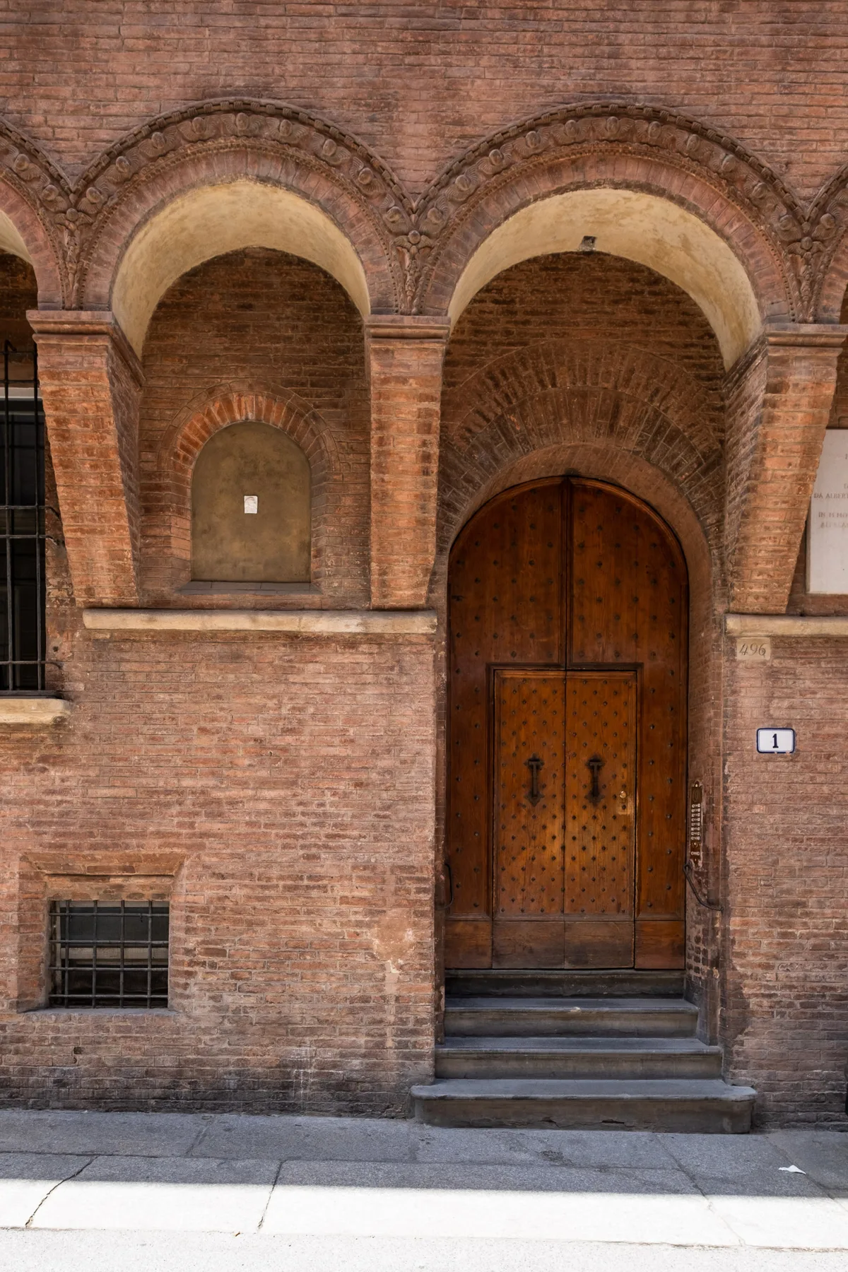 Entrada de un edificio de ladrillo con una puerta de madera arqueada y escalones de piedra.