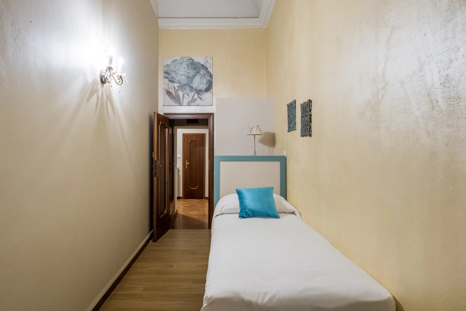 Un dormitorio estrecho con una cama individual y una almohada azul.