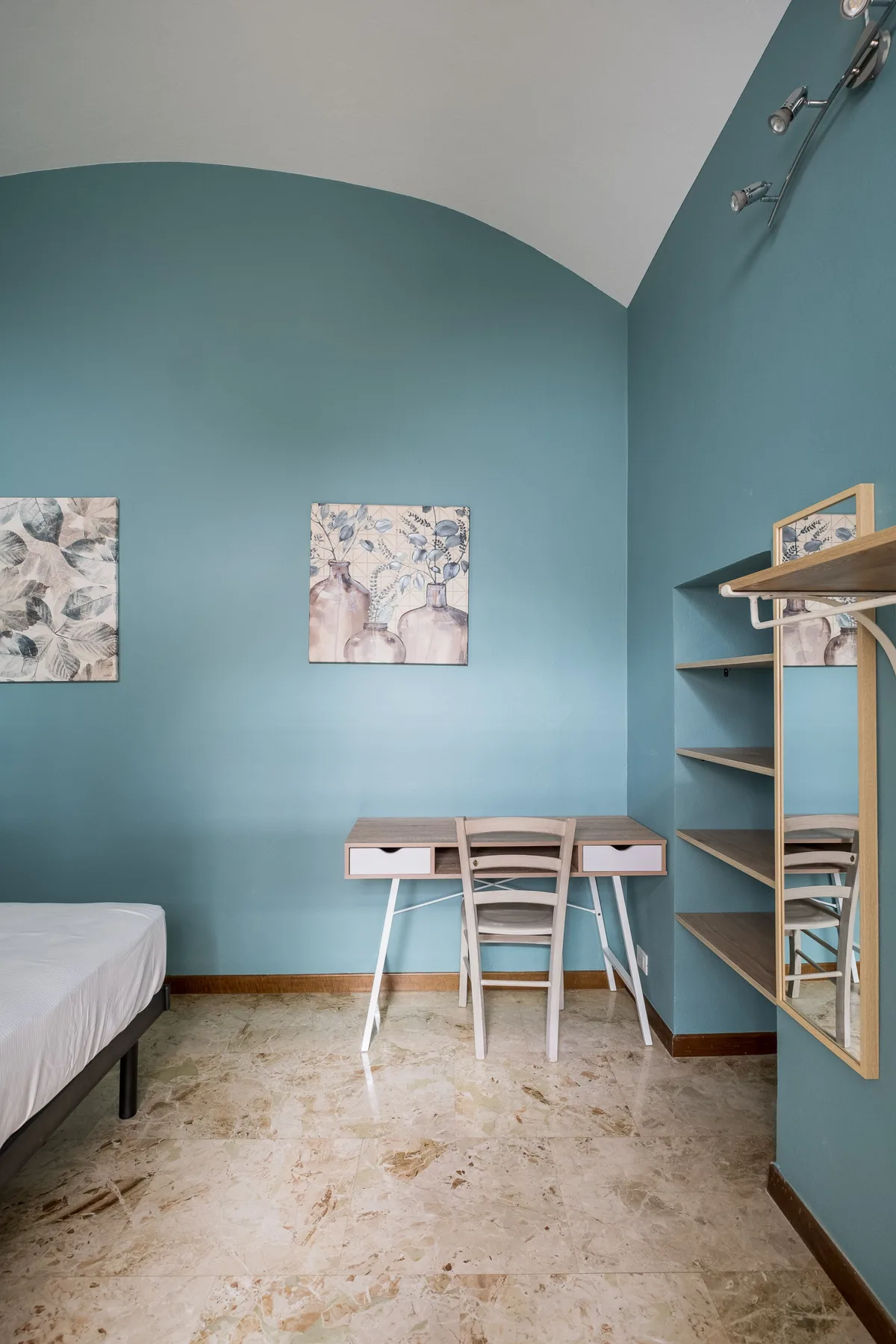 Dormitorio con cama, escritorio y estanterías empotradas junto a paredes de color verde azulado.