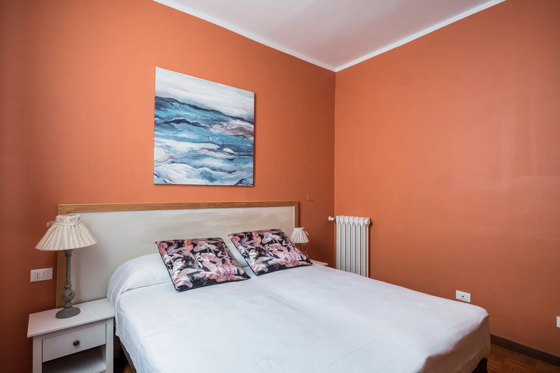 Un dormitorio con una cama, cojines de colores y un cuadro en la pared.