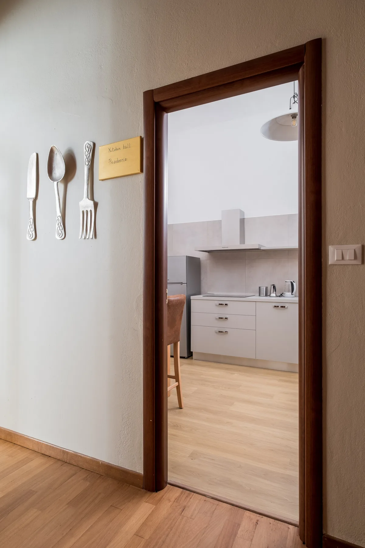 Una puerta da a una cocina con gabinetes claros y piso de madera.