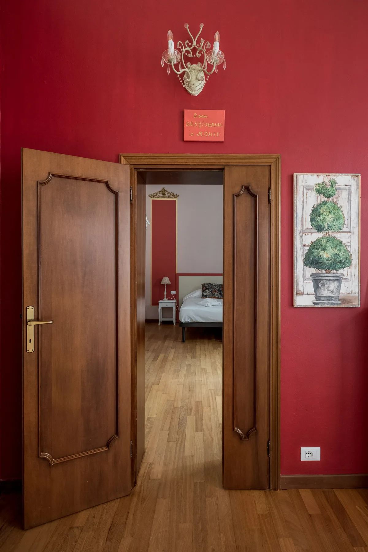 Un pasillo de paredes rojas da a un dormitorio con una cama y suelo de madera.