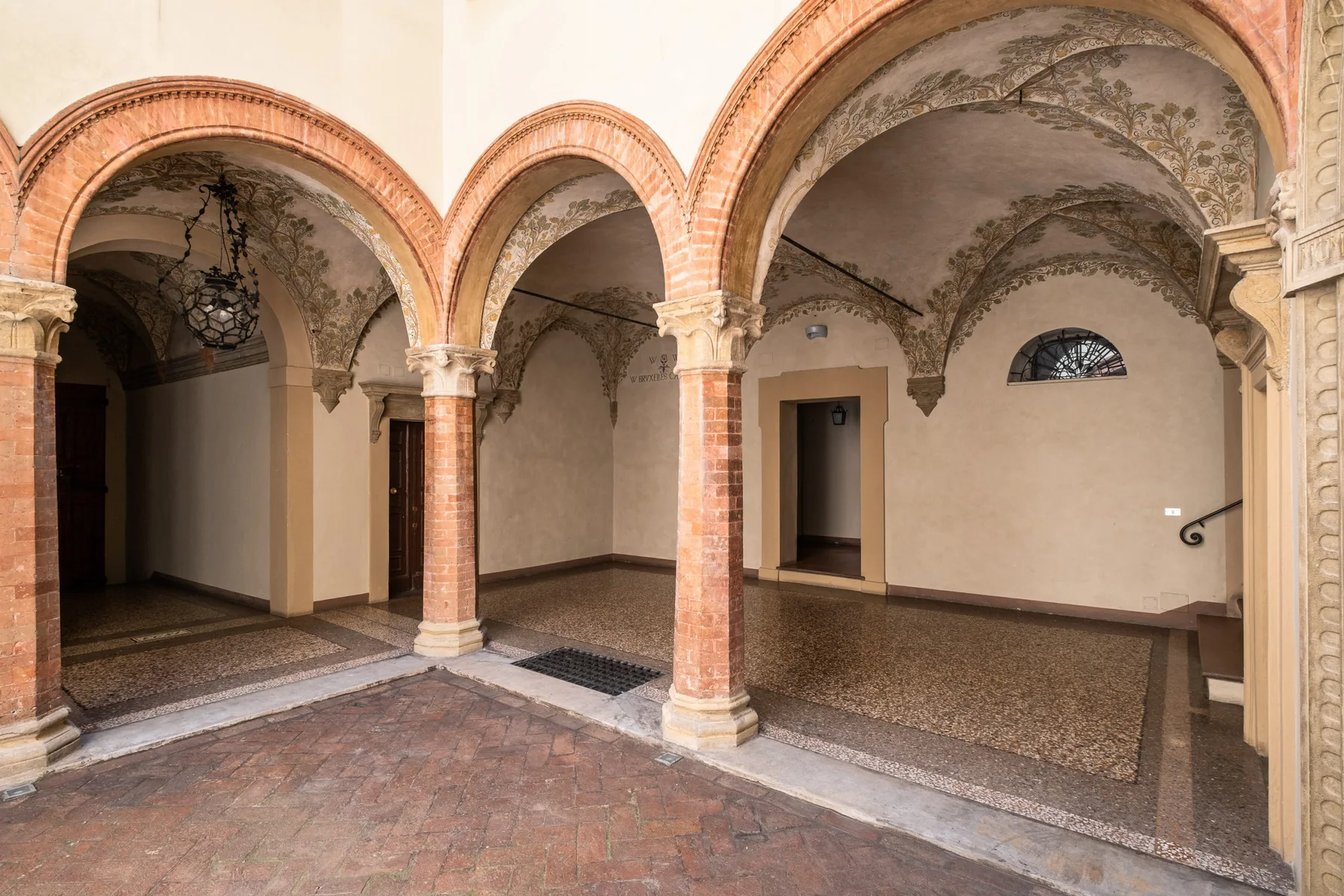 Un patio interior con arcos, columnas de ladrillo y suelo estampado.