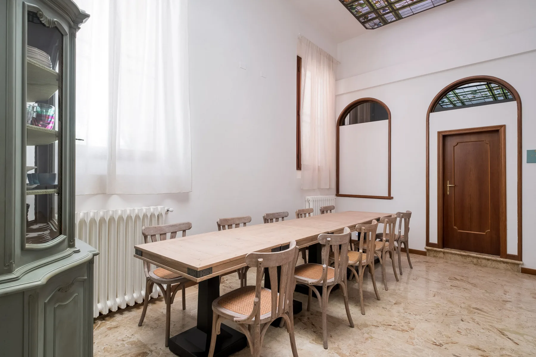 Un comedor con una mesa larga y sillas bajo ventanas altas.