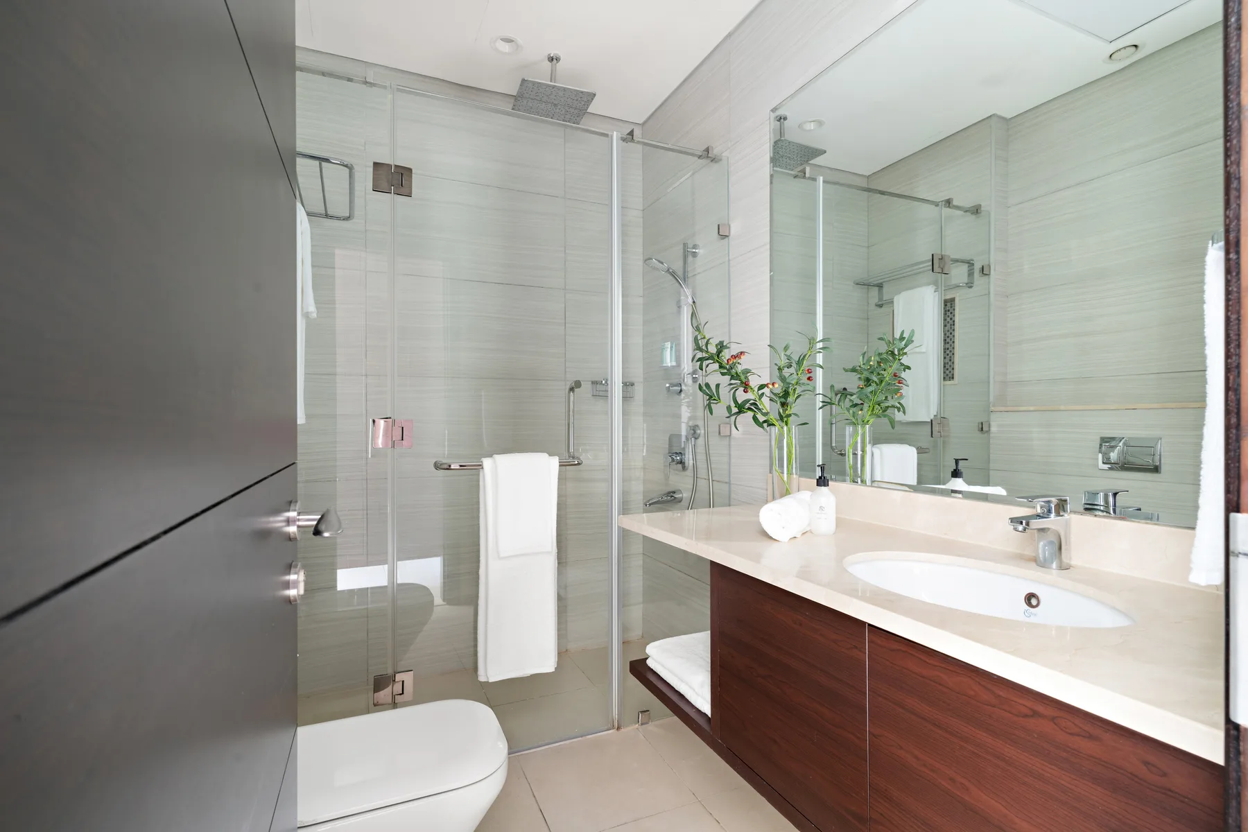 Un baño luminoso con azulejos, ducha de vidrio y un amplio lavabo.
